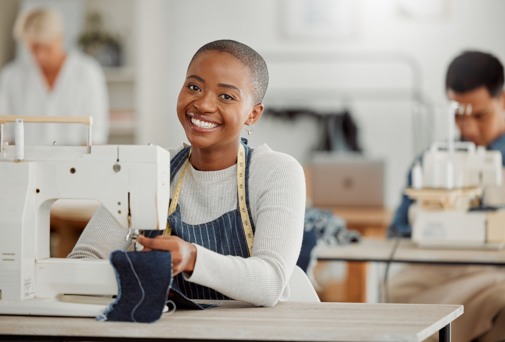 Happy, creative black fashion student or designer sitting and smiling in class by a sewing machine
